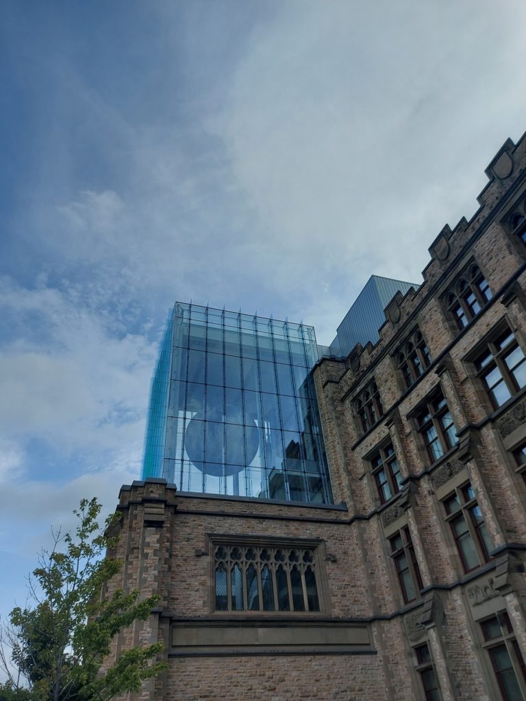 A view from the side of the central glass facing of the Canadian Museum of Nature, which is an old stone building with stained glass windows. There is a model of the moon suspended from the ceiling visible through the glass.