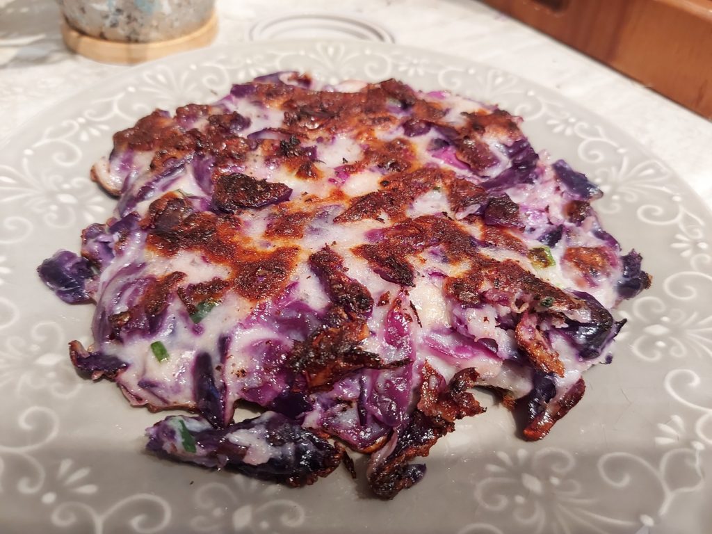 Close up of a freshly pan-fried okonomiyaki, bright purple because of the red cabbage used to make it.