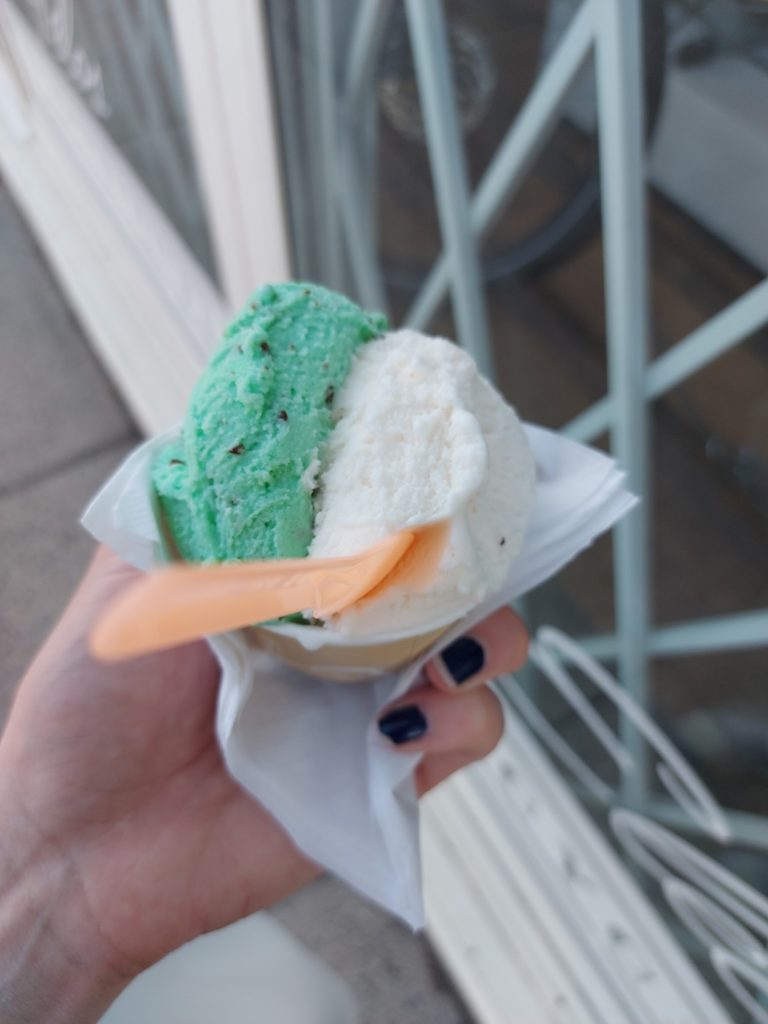 My hand holding a cup with two scoops of gelato in it; bright mint green on the left and a soft rosewater cream on the right.