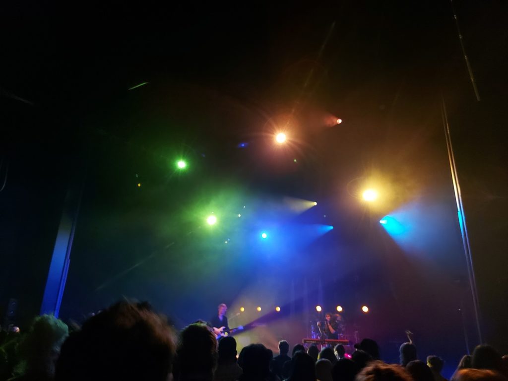 View of the members of Mother Mother on stage, lit up in rainbow-coloured lights.