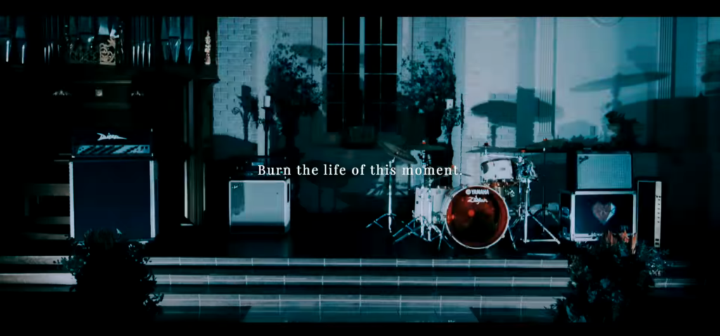 A shot of the band's equipment set up at the front of a chapel, over which is written the phrase, "Burn the life of this moment."