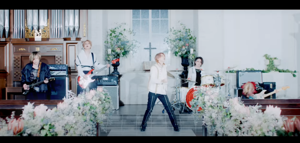 All five band members are bathed in bright white light at the front of a chapel; Saga's bass is bursting with reflected light.