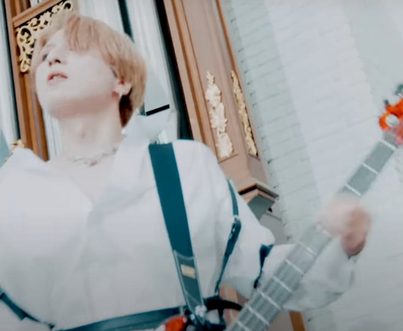 Saga plays bass, bathed in white, looking off towards the left in the midst of a vocal harmony.